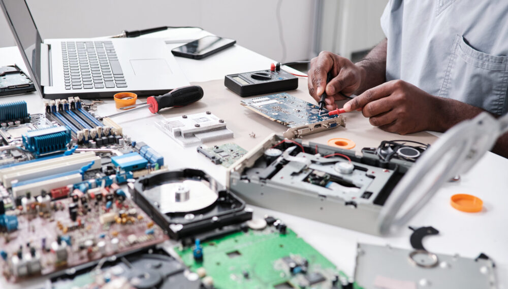 Hands of young African man repairing circuit board Hands of young African man repairing circuit board with soldering iron while sitting by desk in front of laptop by pressmaster